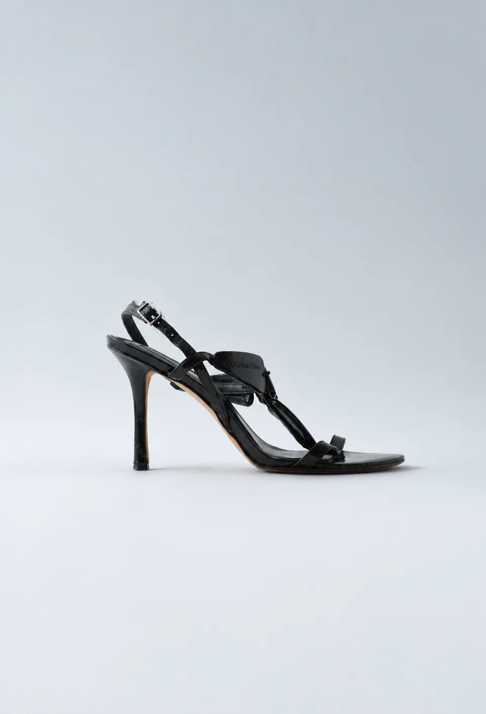 Black patent-leather Calvin Klein stiletto sandal with crossover straps, side profile.